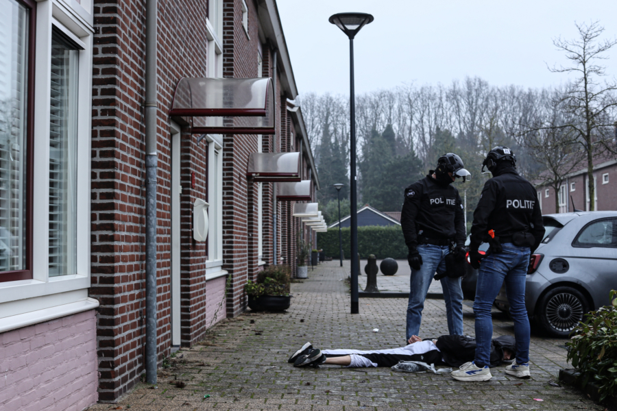 Two police offers stand over an arrested man laying on the floor.